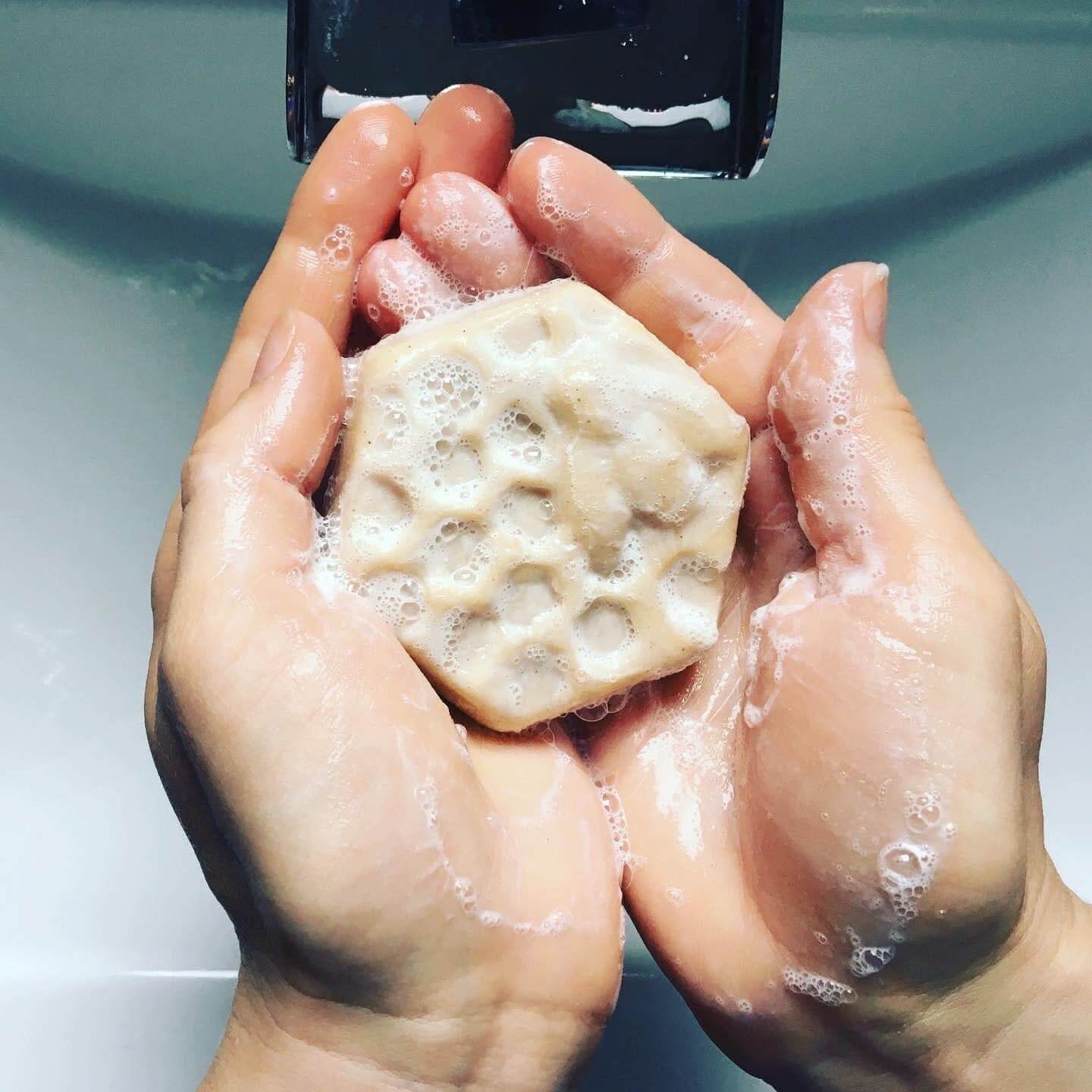 Hands lathering a soap bar under running water, demonstrating hydration for curly hair.