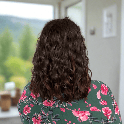 Back view of woman with thick, curly hair in a floral top, showcasing frizz-free, hydrated curls.
